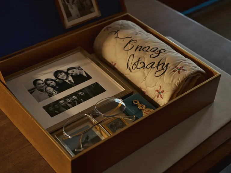 An open keepsake box holding framed family photographs and a folded quilt